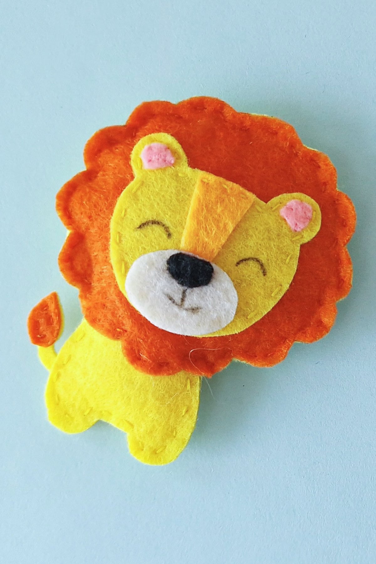 Finished felt lion plush at an angle showing its orange mane, yellow body, and tufted tail