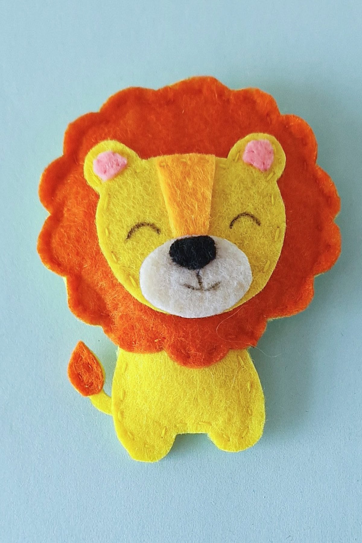 Finished yellow felt lion plush with orange mane and small orange tail tuft