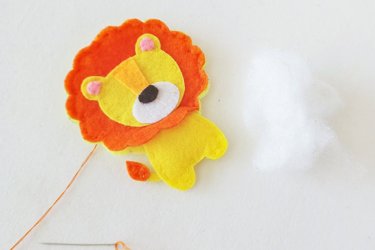 Orange felt mane being stitched to the lion body with stuffing nearby