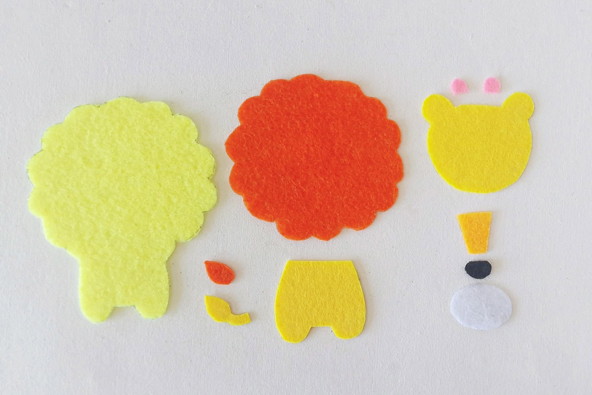 Cut yellow, orange, pink, white, and black felt pieces arranged for the lion plush