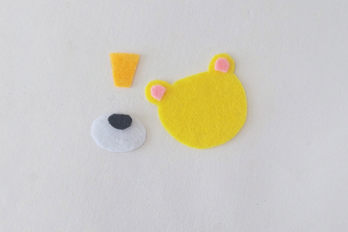 Pink inner-ear pieces and black nose placed on yellow felt head and white muzzle